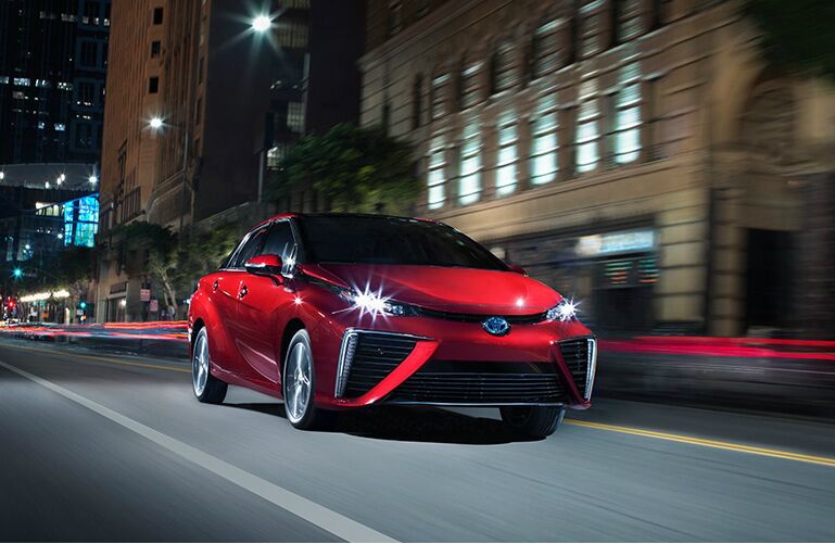 Red 2019 Toyota Mirai drives down a city street at night.