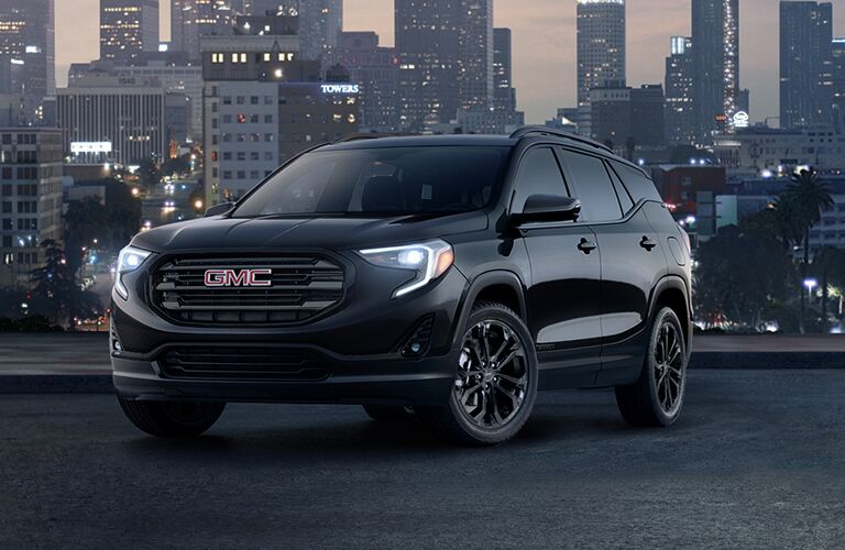 2019 GMC Terrain exterior shot black edition with LED headlights on with a city skyline at night in the background