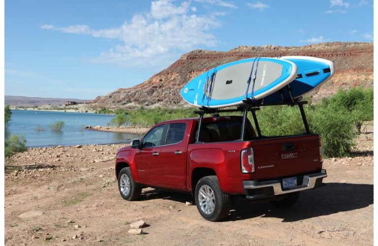 2019 GMC Canyon pickup truck exterior rear shot with red paint color parked on a dirt beach of cliffs near a lake of water