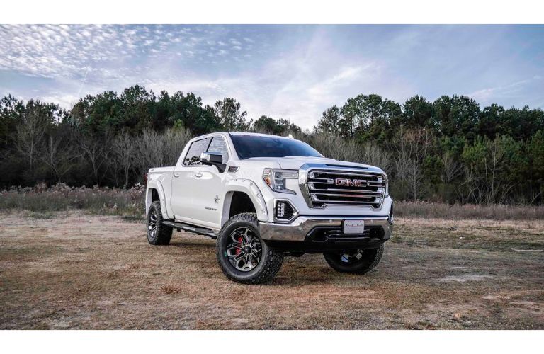 2019 GMC Sierra Black Widow with white paint job exterior shot parked on a dry grass field near fields of brush and a blue sky