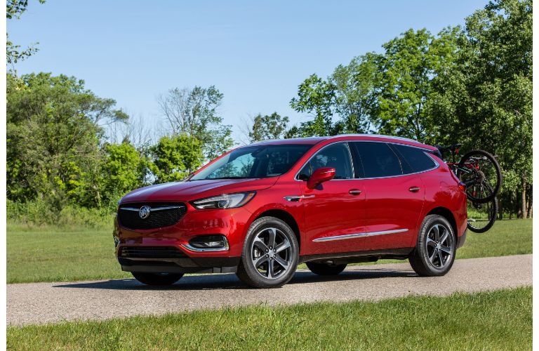 2020 Buick Enclave Avenir exterior front shot with dark red paint color driving on a forest park road with bikes attached to its back