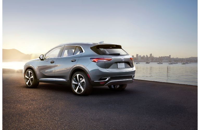 2021 Buick Envision exterior rear shot with metallic paint color parked on a beach near boating docks and a bright sun