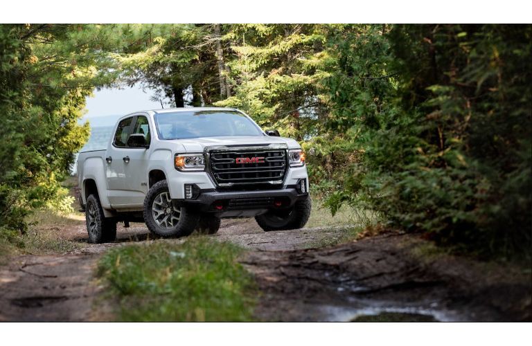 2021 GMC Canyon AT4 exterior shot with white paint color driving down a dirt road in a forest