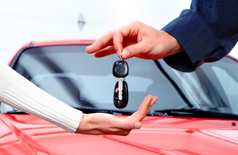 a car delivery salesman handing over the car keys and key fob to a new vehicle owner