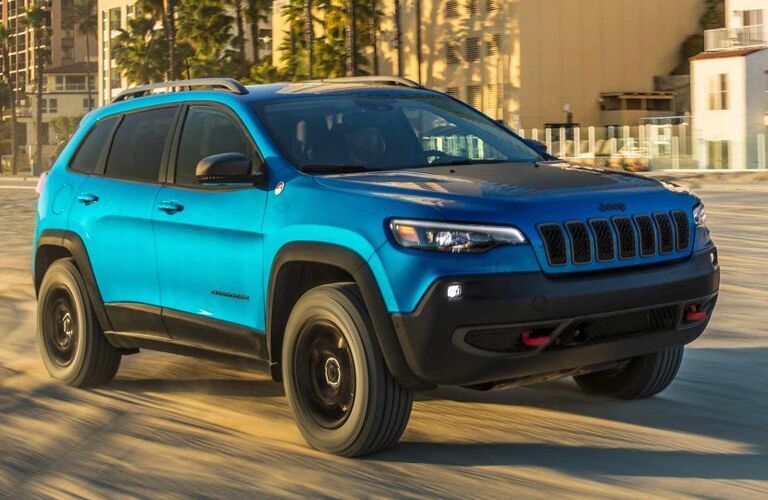 2019 Jeep Cherokee exterior shot with blue teal paint color driving on a beach near palm trees and beachfront property