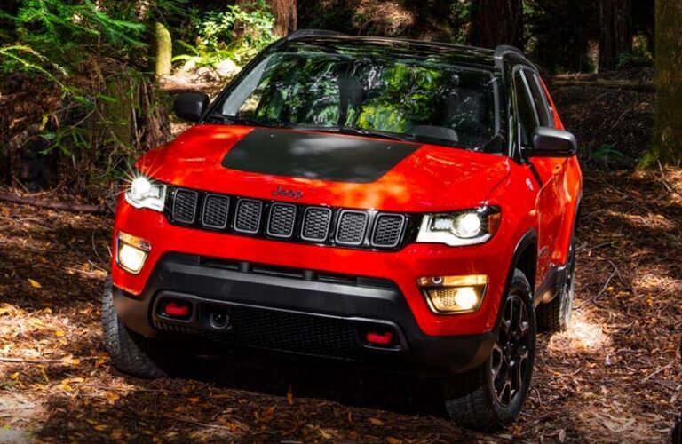 2019 Jeep Compass exterior front shot with red and black paint color driving through a dirt off-road forest path