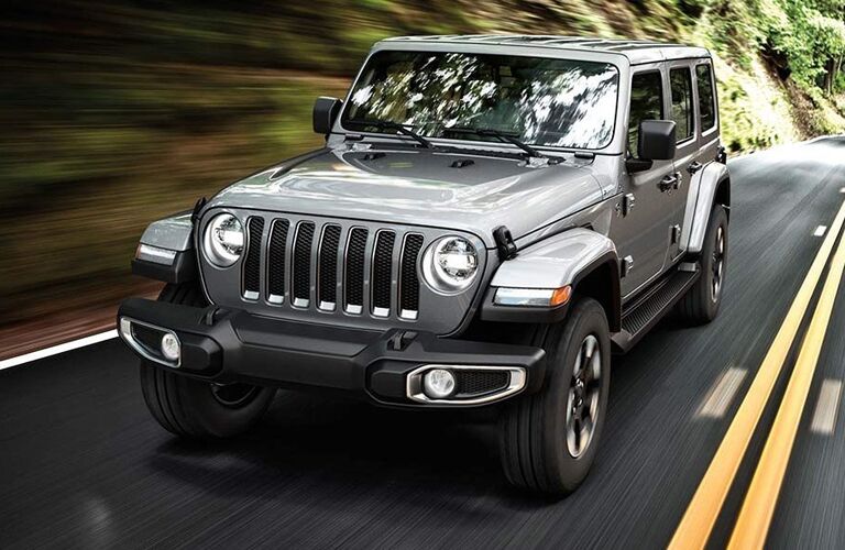 2019 Jeep Wrangler exterior front shot with gray metallic paint color driving alongside a grassy cliff on a highway