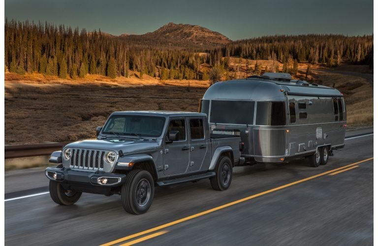 2020 Jeep Gladiator exterior shot with gray metallic paint color towing a trailer on a country road near a forest