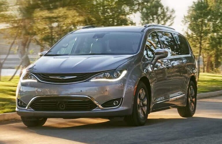 2019 Chrysler Pacific minivan exterior shot with silver metallic paint color driving through a forest park in the summer