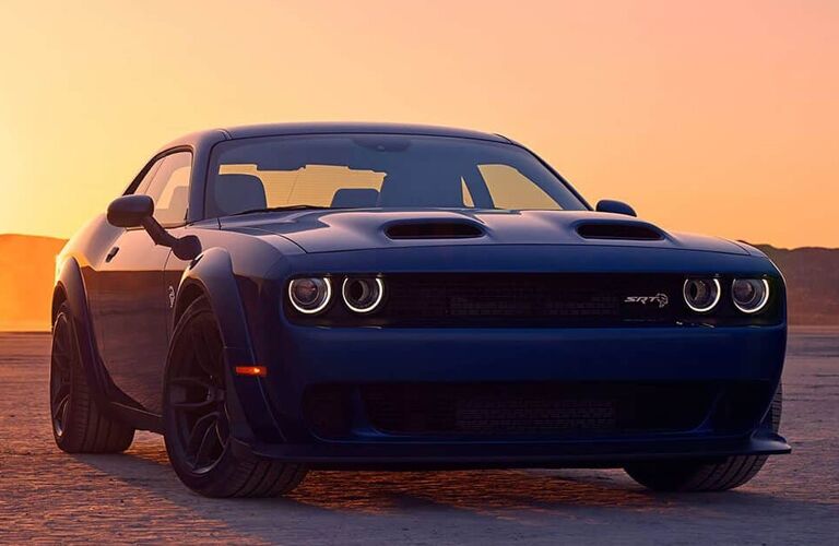 2019 Dodge Challenger exterior front shot with blue paint color parked on dry cracked earth as the sun sets in an orange sky