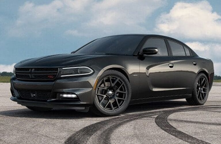 2019 Dodge Charger exterior side shot with dark gray paint color parked on an empty lot near tread drifting marks with clouds in a blue sky behind it