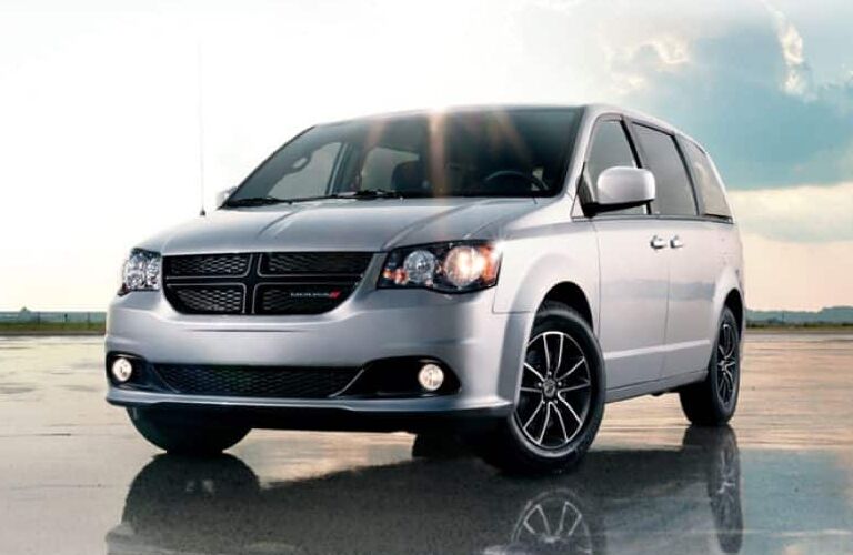 2019 Dodge Grand Caravan exterior shot with silver paint color parked on the wet sand of a beach under a bright sun