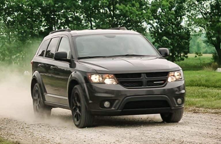 2019 Dodge Journey exterior shot with black paint color driving on a gravel road in a forest as dust kicks up from the wheels
