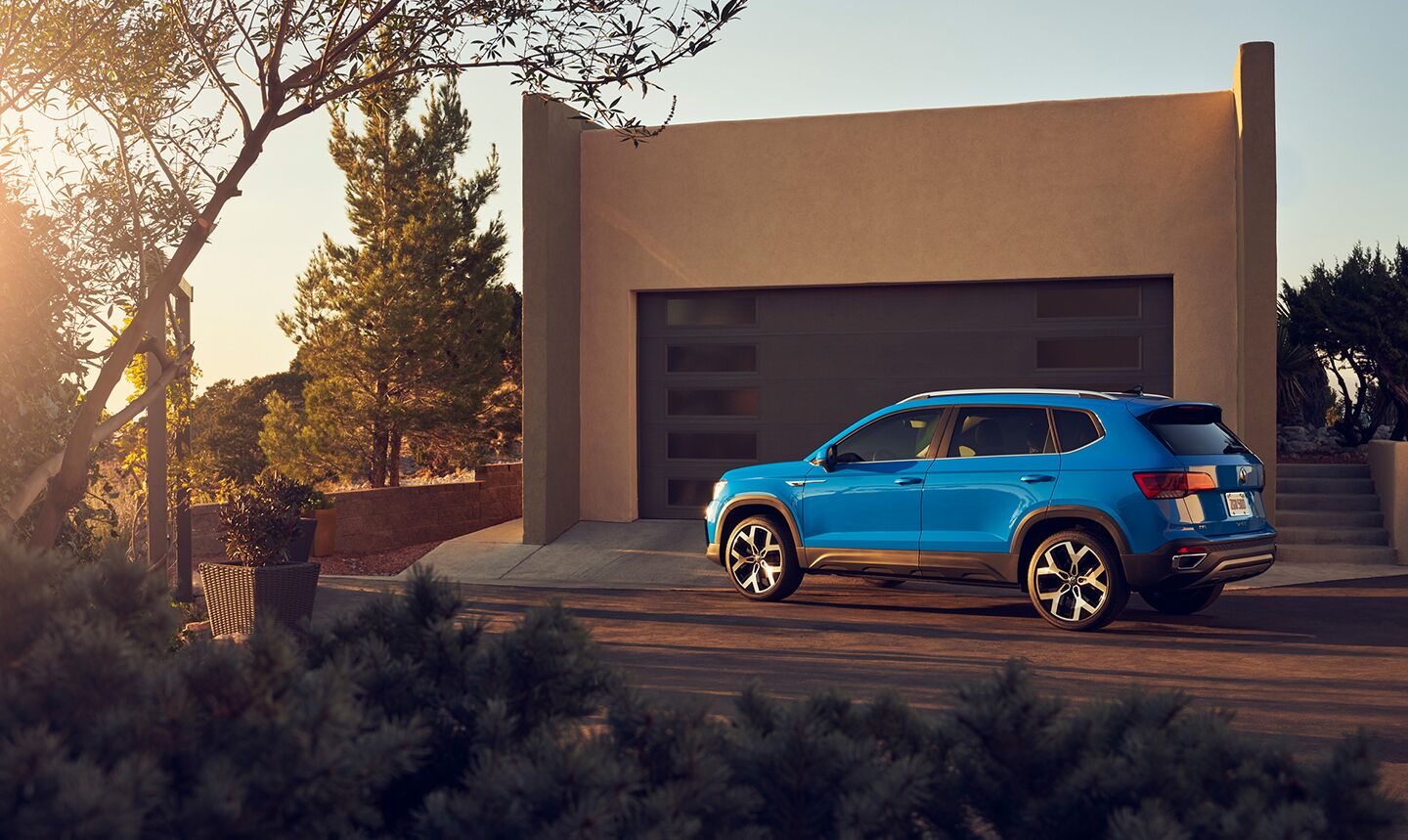 A VW Taos parked in front of a modern home at sunset.