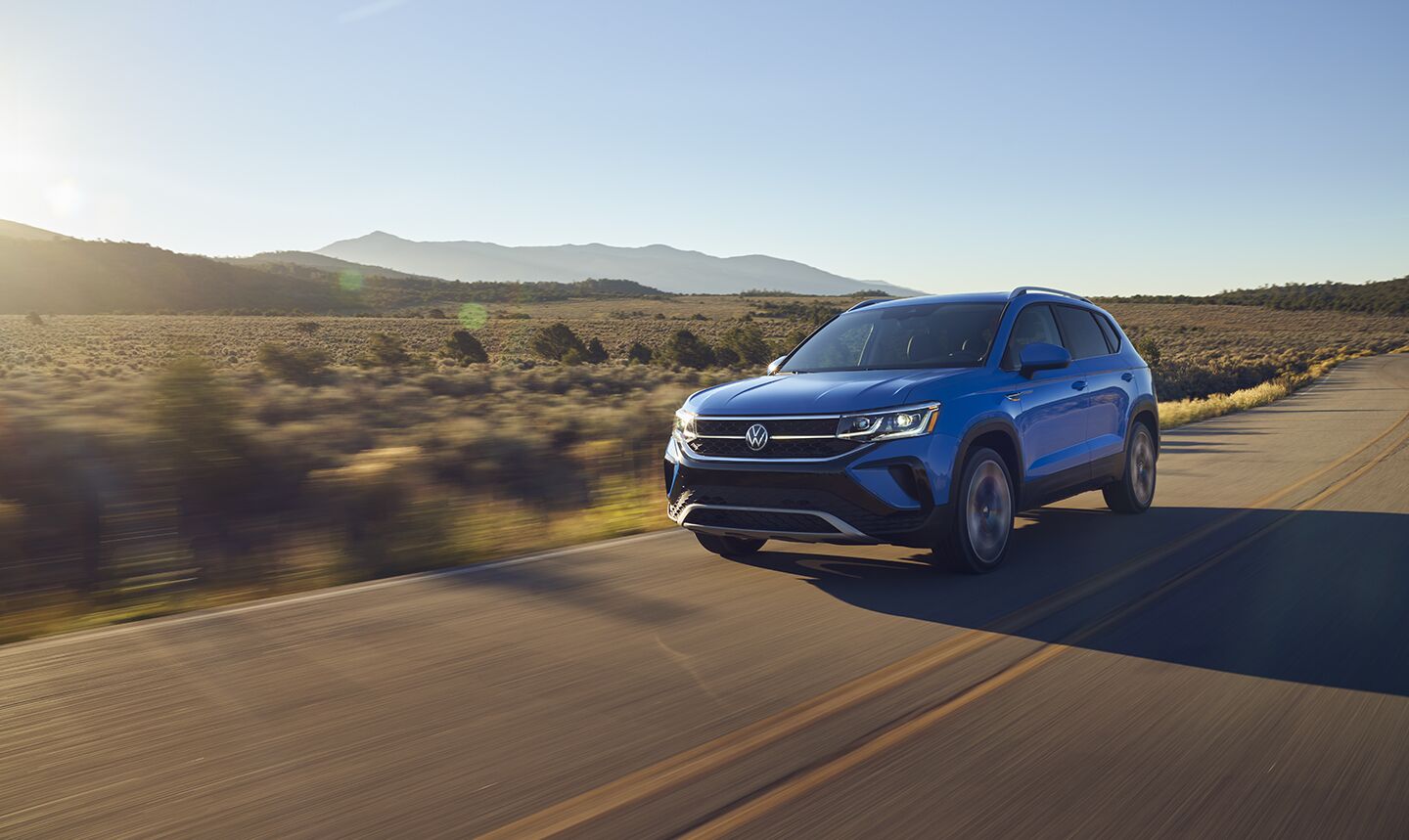 A VW Taos drives on a two-lane highway with mountains in the distance.